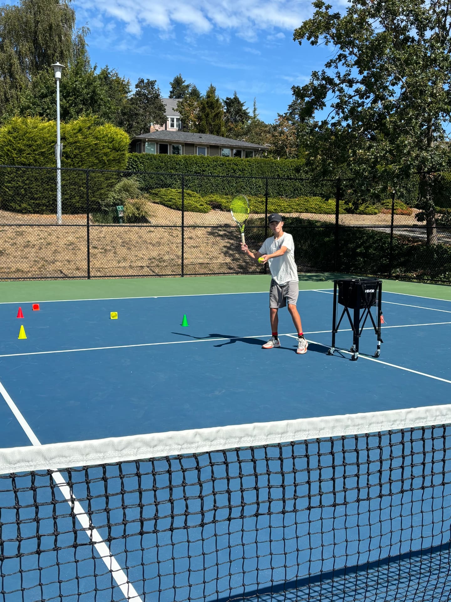 Private tennis lesson set up with cones and a ball cart on a Victoria court